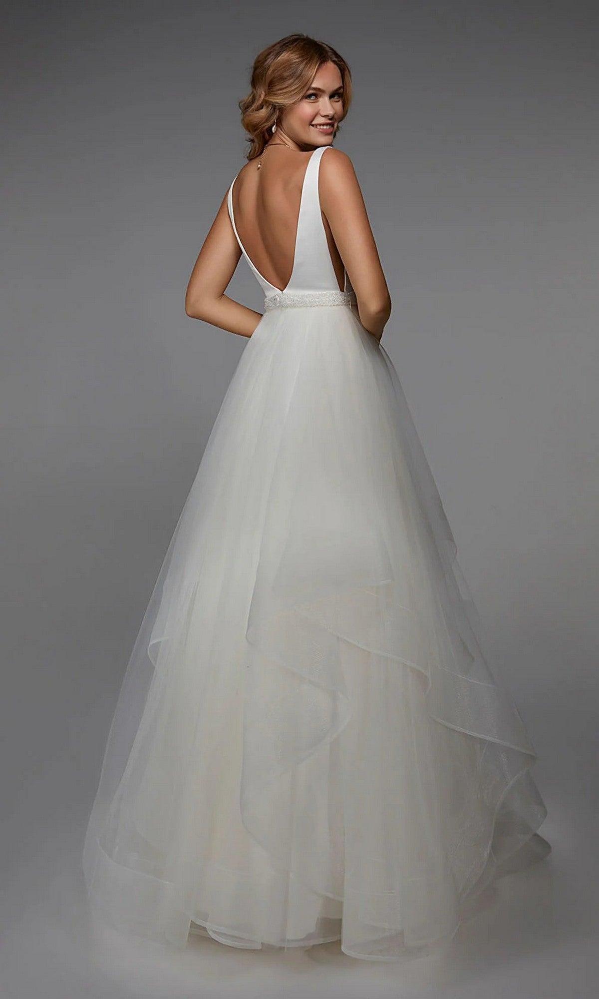 A woman in the Alyce 7022 Long White Dress with a sleeveless top, beaded waistband, and A-line tulle skirt stands facing away, glancing over her shoulder.